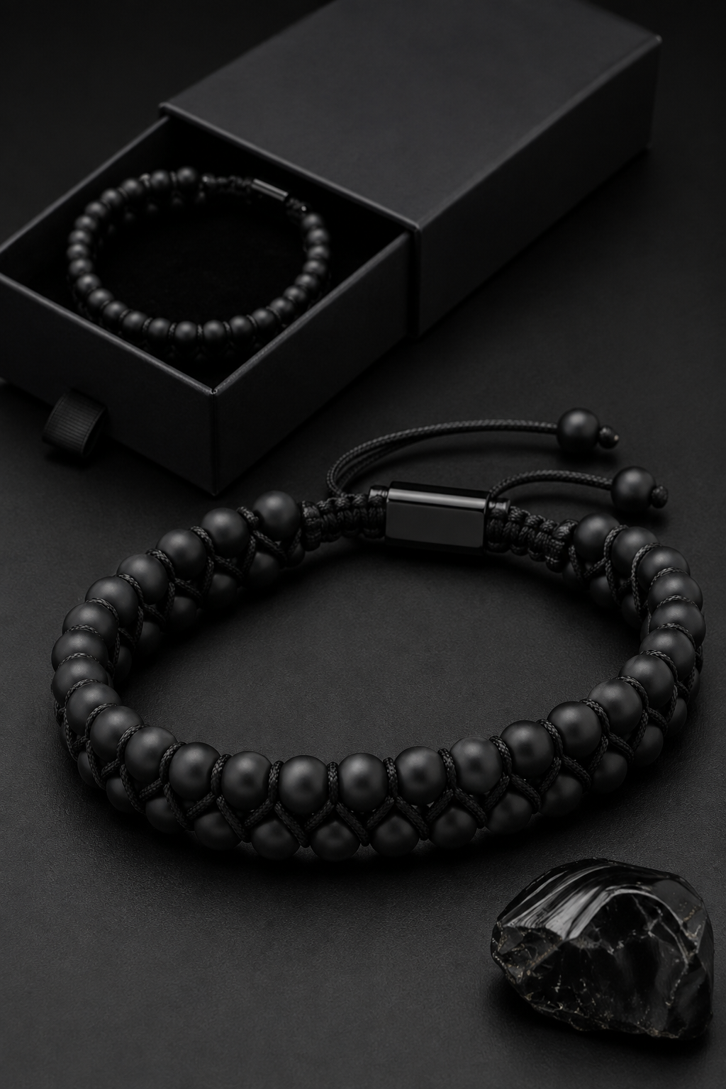 Black GT Collection onyx beaded bracelet with adjustable cord displayed beside a black jewelry box and black stone.