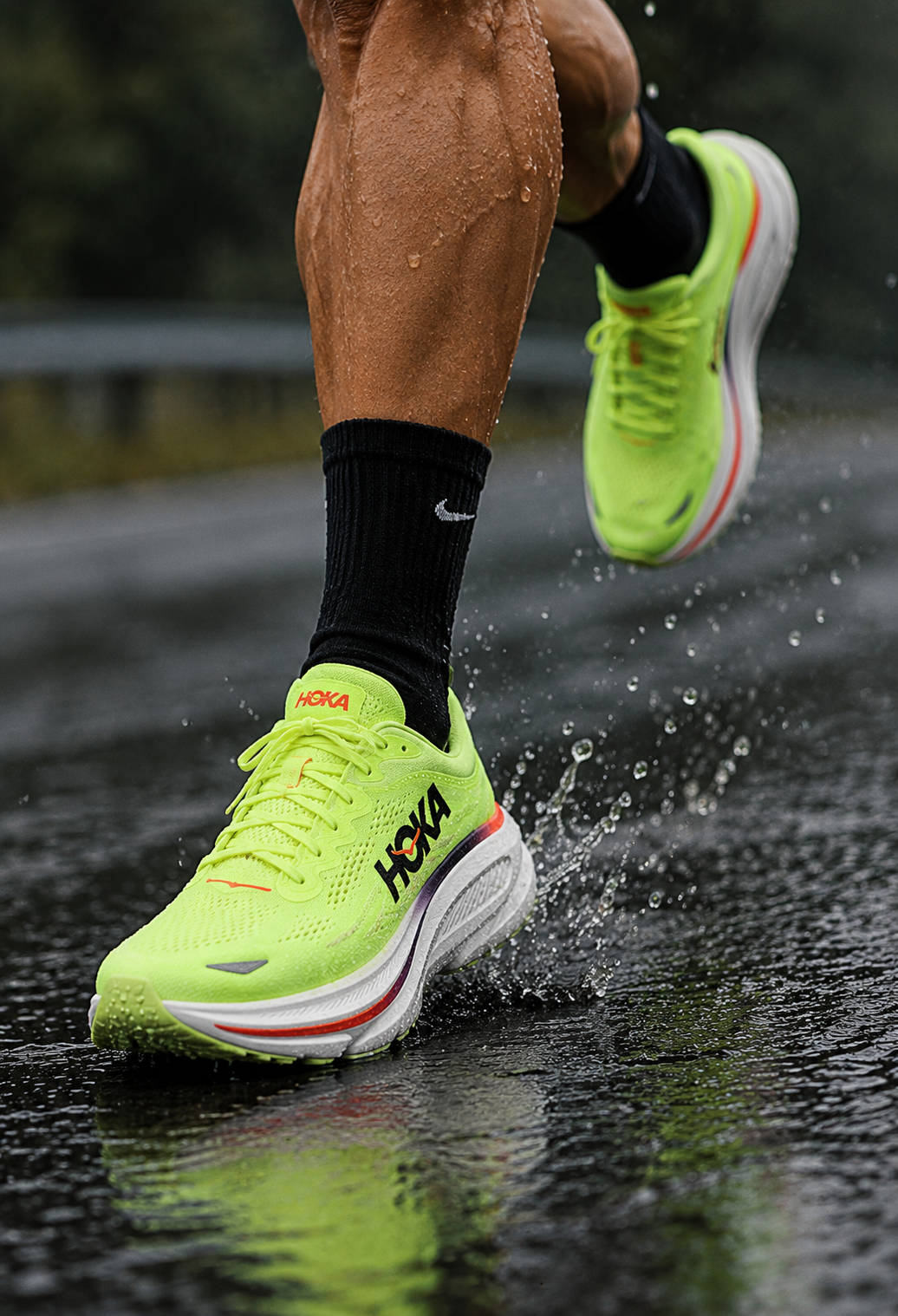Neon HOKA running shoes worn during a rainy road run, showing the cushioned sole and bright performance upper.