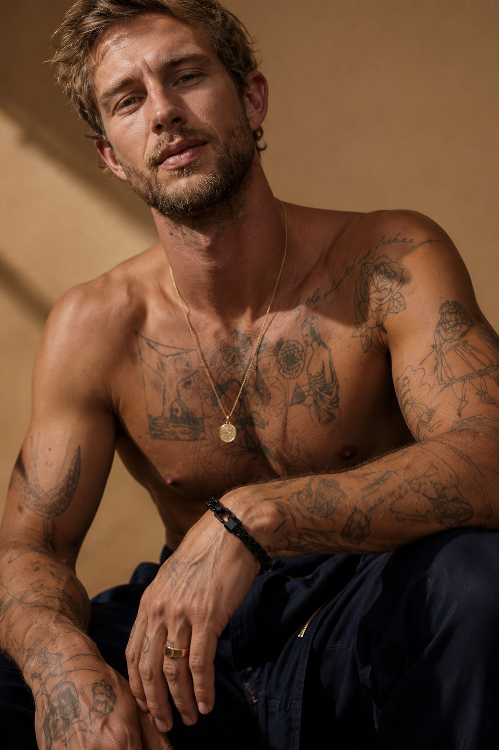 Tattooed man wearing a sleek black chain bracelet with a dark metal clasp in a warm editorial fashion setting.