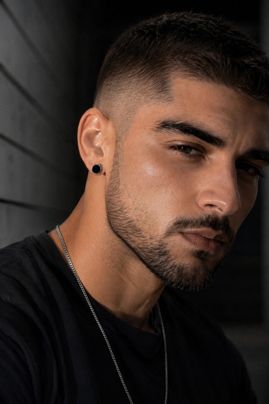 Man wearing minimalist black round stud earrings with a black T-shirt and silver chain for a modern masculine look.