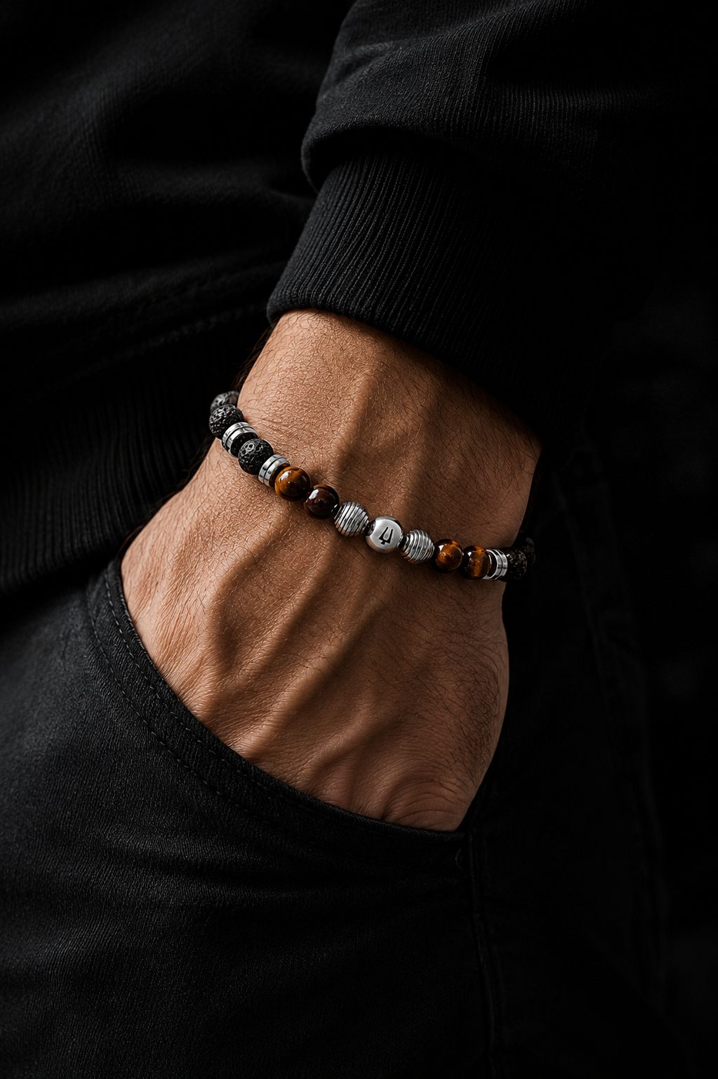Close-up of a man wearing a black lava stone and brown tiger-eye beaded bracelet with polished silver accents and black clothing.