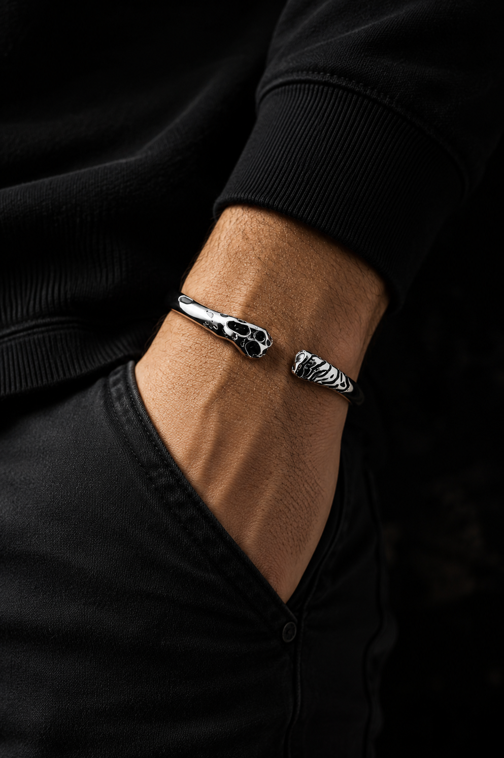 Close-up of a man wearing a polished silver open cuff bracelet with contrasting animal-inspired ends and an all-black outfit.