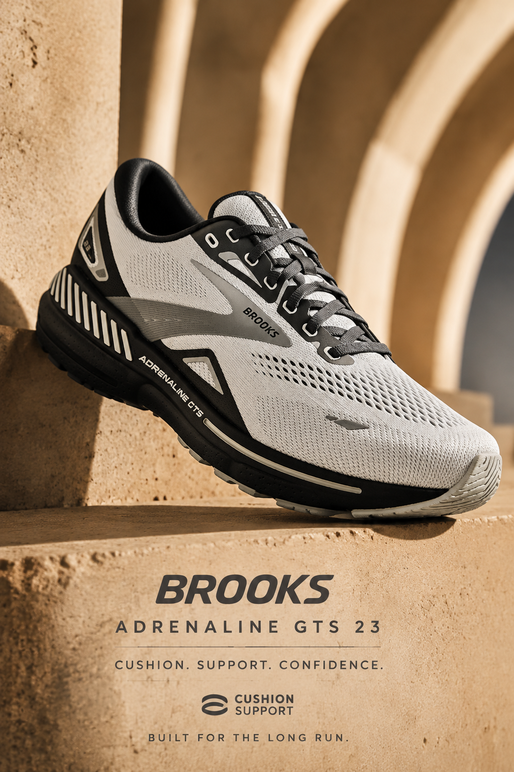 A Brooks Adrenaline GTS 23 men's running shoe in white, grey, and black resting on a textured, sandy-brown architectural ledge against an archway backdrop. Text at the bottom reads: "Brooks Adrenaline GTS 23. Cushion. Support. Confidence. Built for the long run."