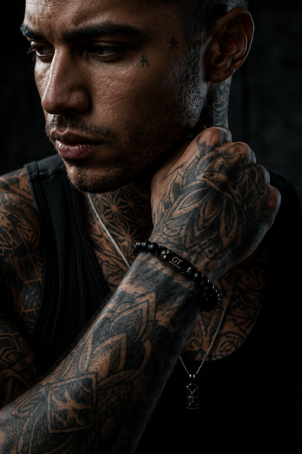 Tattooed man wearing a black GT Collection onyx bracelet with a black tank top in a dark editorial setting.
